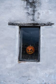 A carved pumpkin with a sinister smile sits behind an old window, creating a spooky Halloween atmosphere.