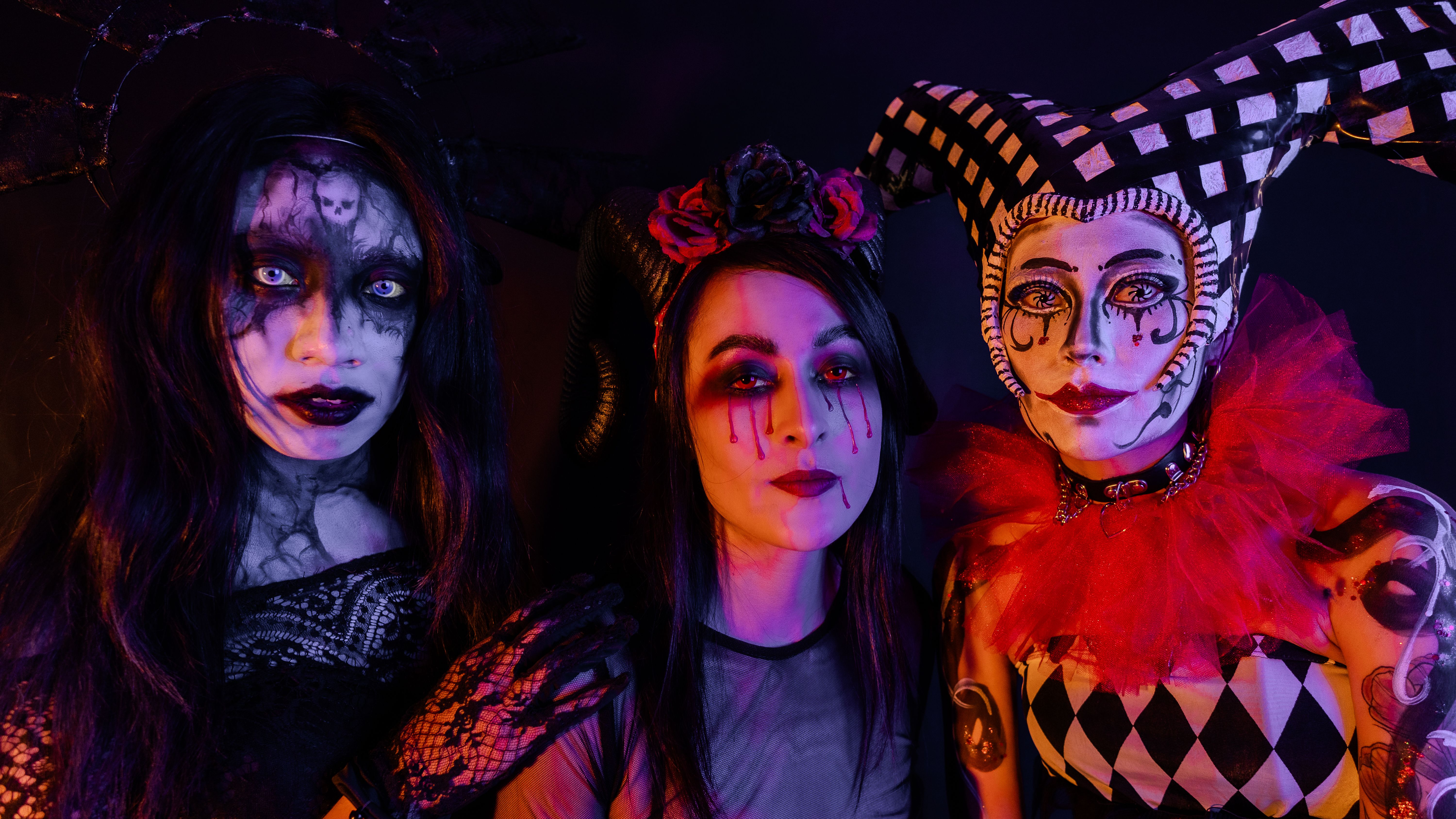 Three individuals in elaborate gothic horror costumes and makeup, evoking a Halloween theme.
