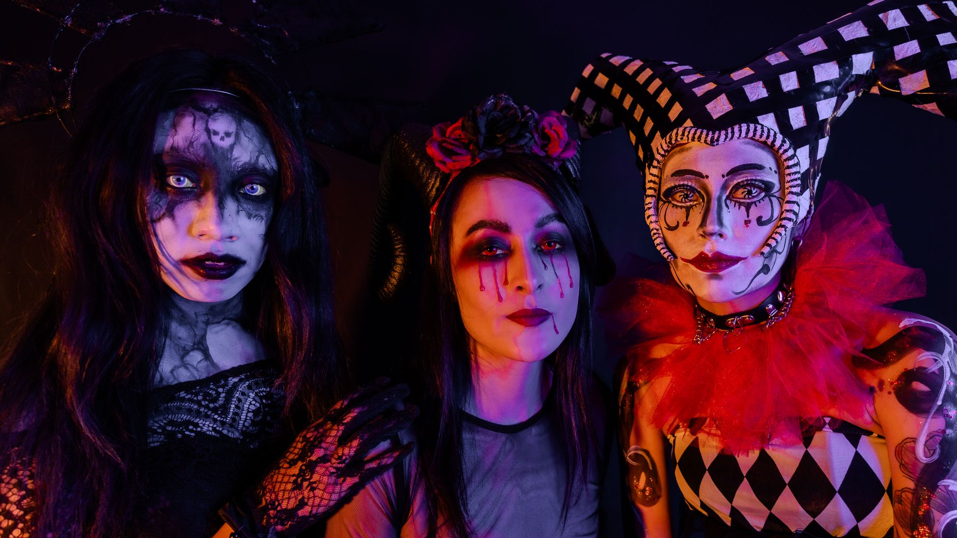Three individuals in elaborate gothic horror costumes and makeup, evoking a Halloween theme.