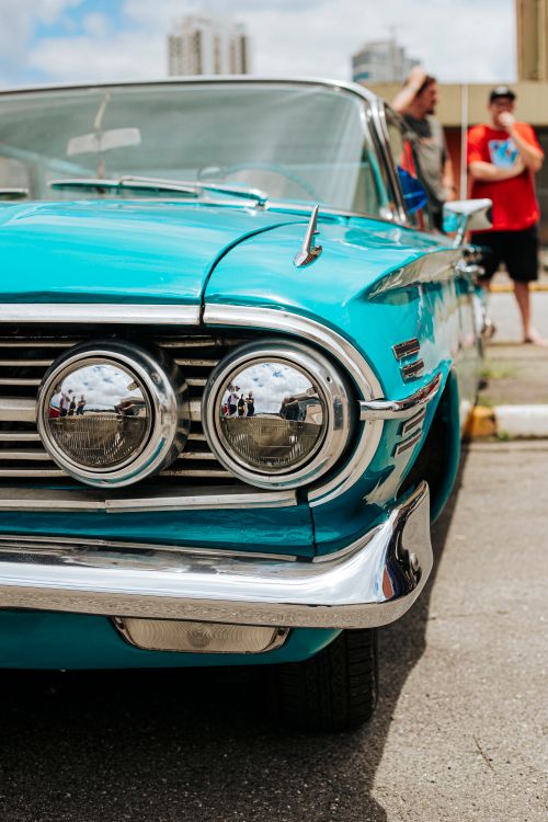 Free Close-up of a vintage blue car with headlights, people in background. Outdoors. Stock Photo