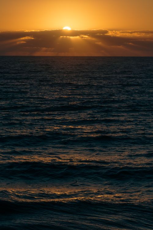 Free A breathtaking sunset casts golden hues over the tranquil ocean waves, creating a serene seascape. Stock Photo