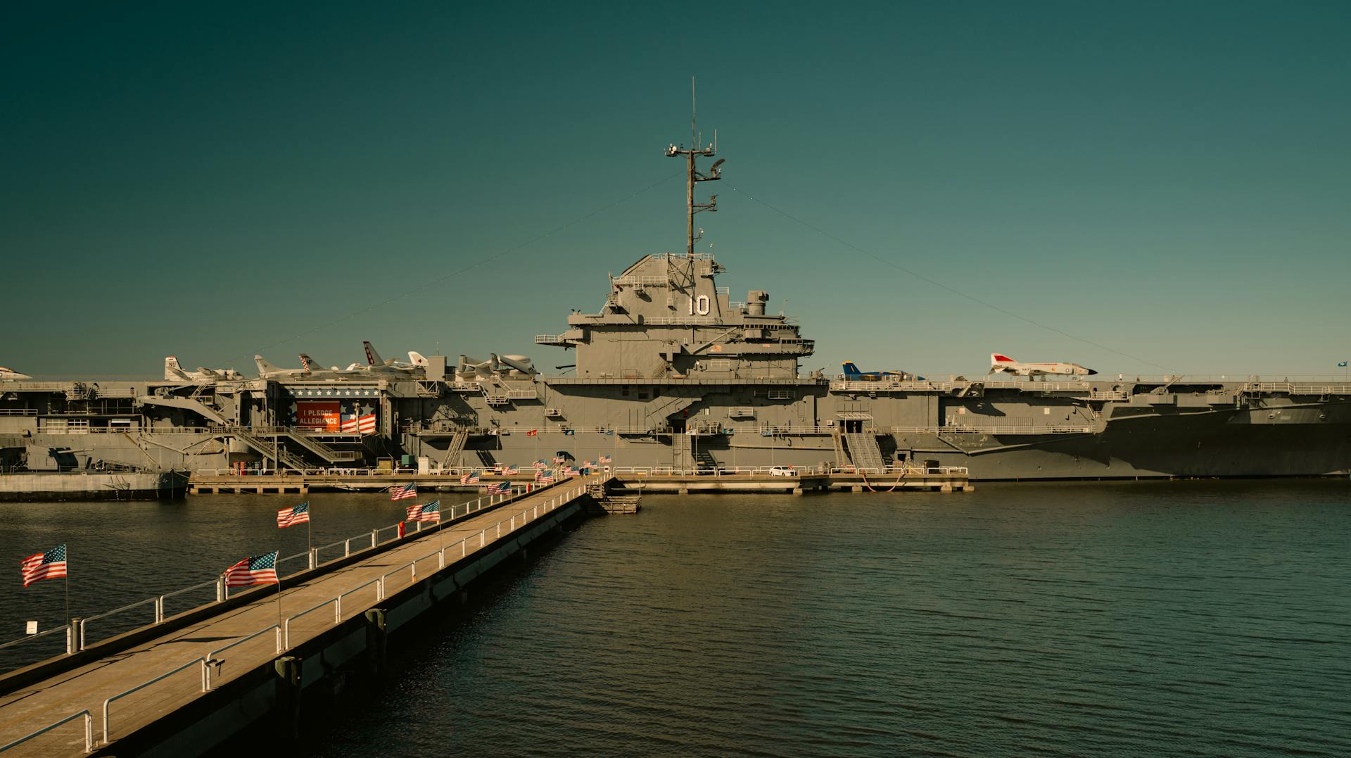 View of USS Yorktown aircraft carrier docked at harbor with walkway and flags.