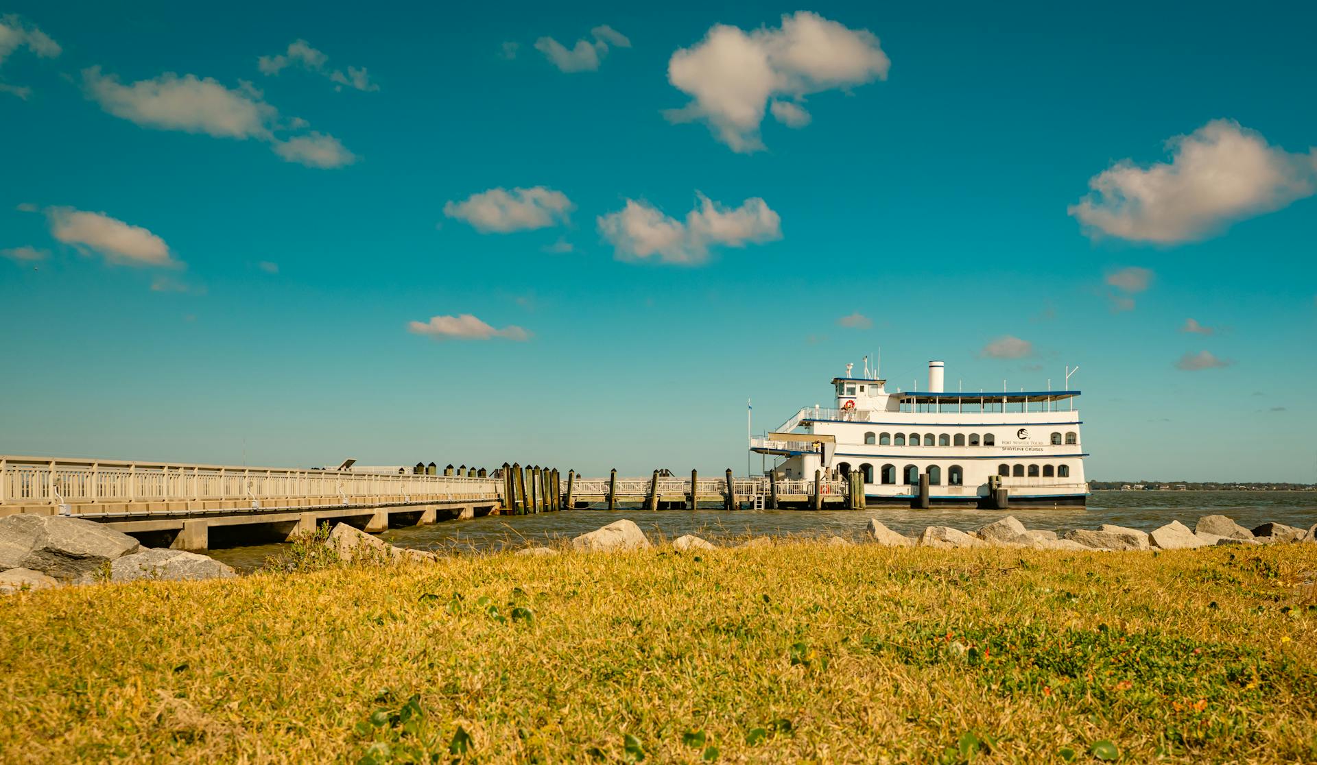 A ferry boat near a wooden dock under a clear blue sky with scattered clouds, captured in bright daylight.