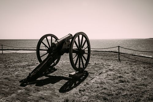 Free Sepia-toned photo of an antique cannon on the waterfront, capturing a timeless military artifact. Stock Photo