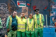 Group of people in Catrina makeup celebrating Day of the Dead in front of urban graffiti.