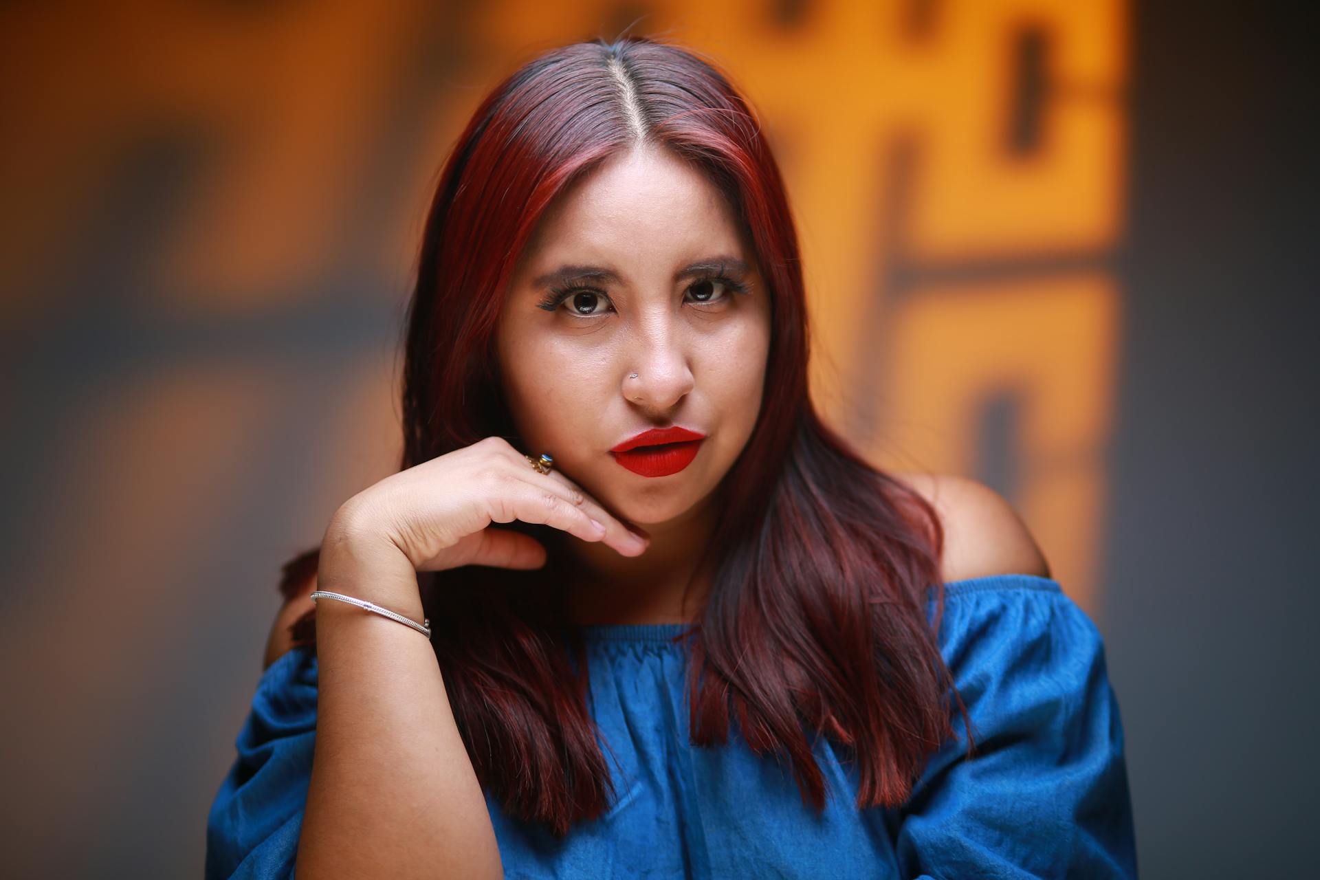 Studio portrait of a woman with striking red lips and vibrant hair, set against a blurred background.