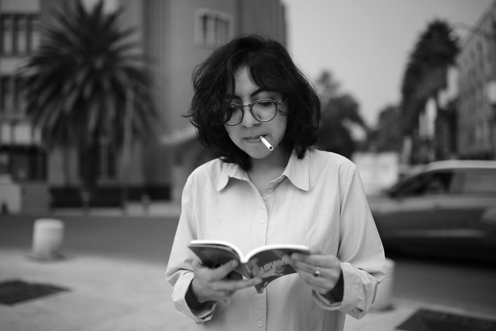 Black and white portrait of a stylish woman reading outdoors in Mexico City, showcasing casual street style.