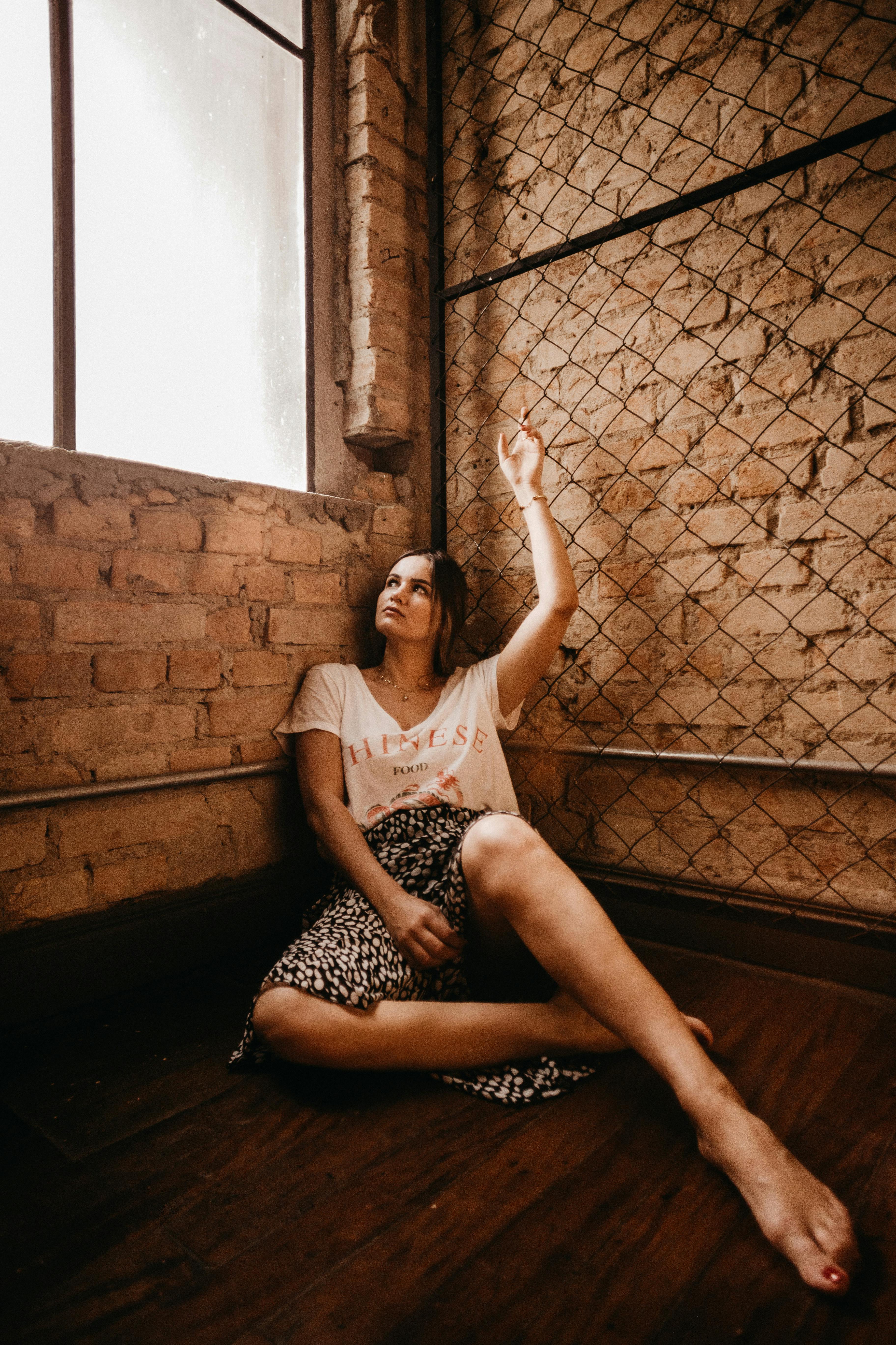 一位穿着休闲装的女性，坐在阁楼裸露的砖墙窗前，陷入了沉思