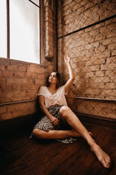 一位穿着休闲装的女性，坐在阁楼裸露的砖墙窗前，陷入了沉思