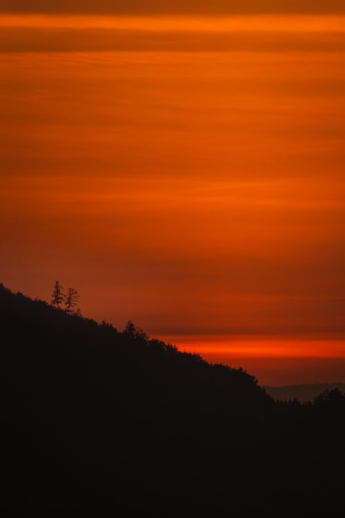 Free Beautiful orange sunset casting silhouettes over the hills of Graz, Austria. Tranquil landscape with serene evening light. Stock Photo