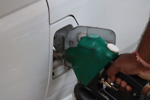 Close-up of a hand refilling a car's gas tank at a station with a green fuel nozzle.
