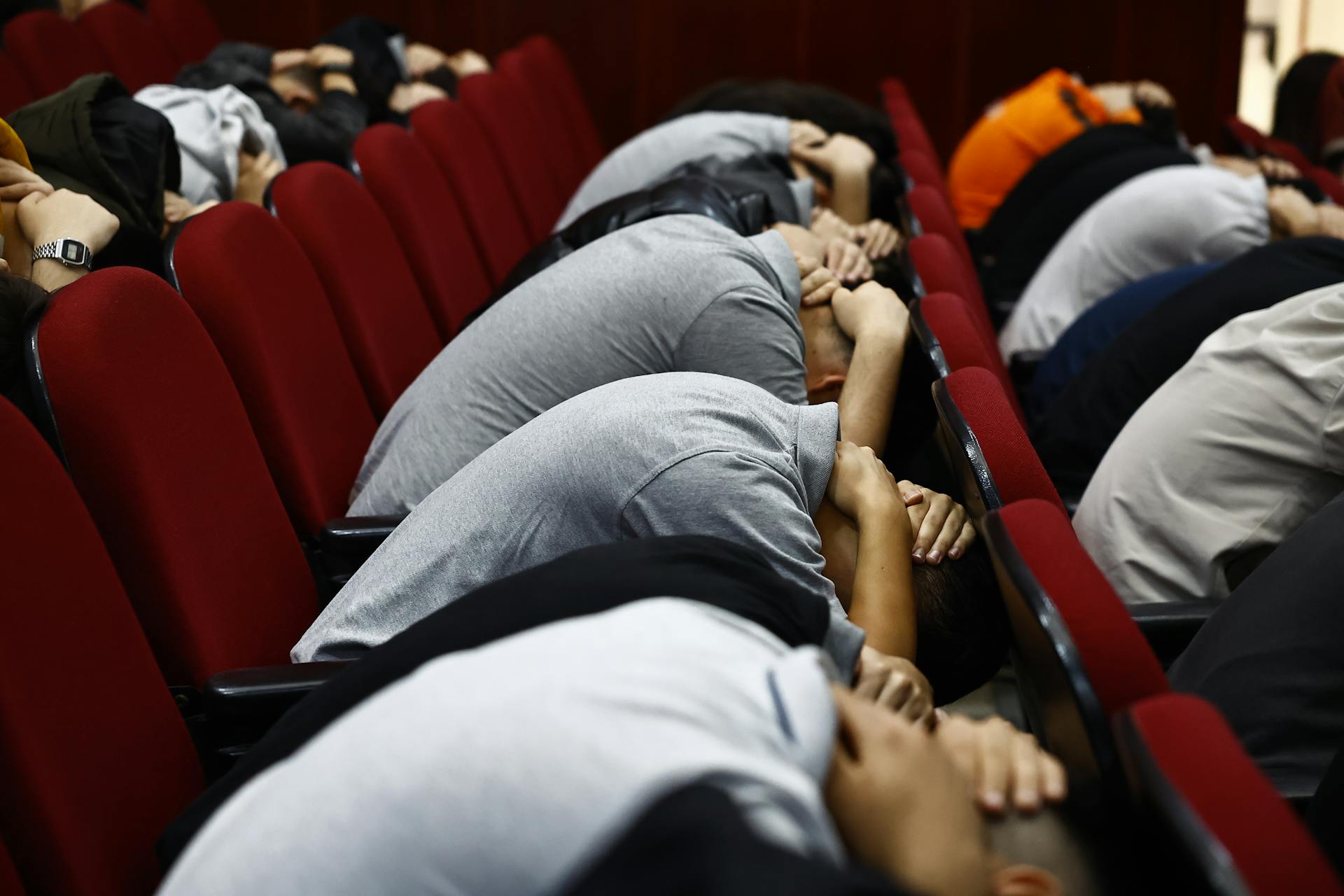 Individuals participate in an emergency drill, simulating earthquake safety procedures in an indoor setting.