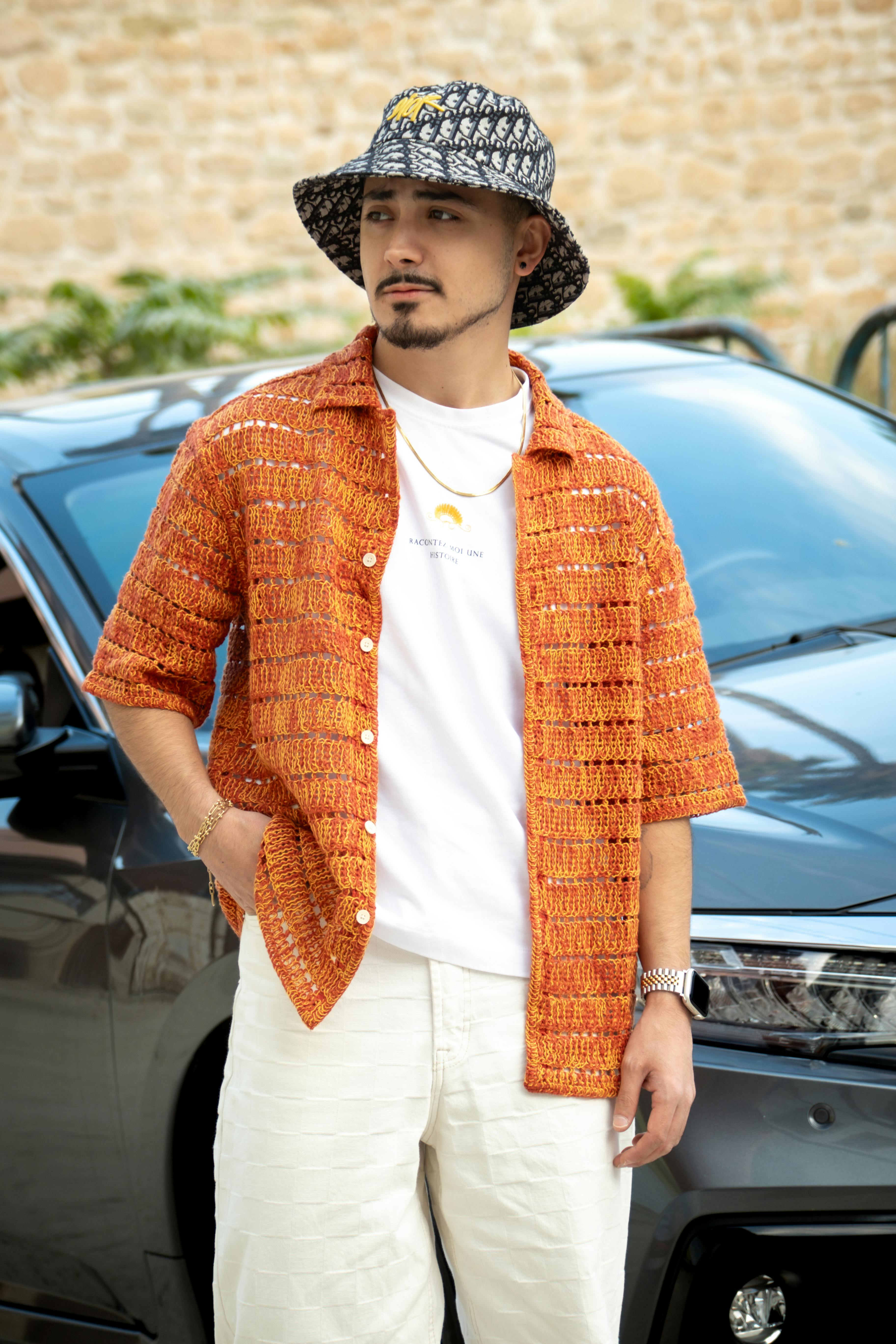 Man in stylish orange shirt and hat standing outside by a car