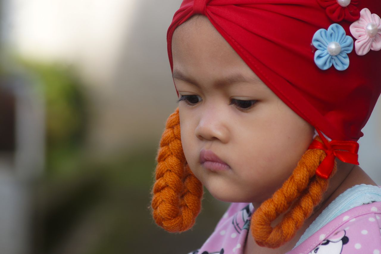 a focused portrait of a child wearing a red headwrap with braids and f