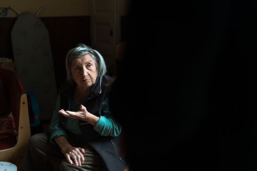 Free An elderly woman gestures thoughtfully while seated in a dimly lit room in Prague, Czechia. Stock Photo