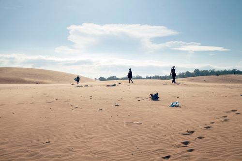Free A serene desert scene with three people walking across sandy dunes under a clear sky. Stock Photo