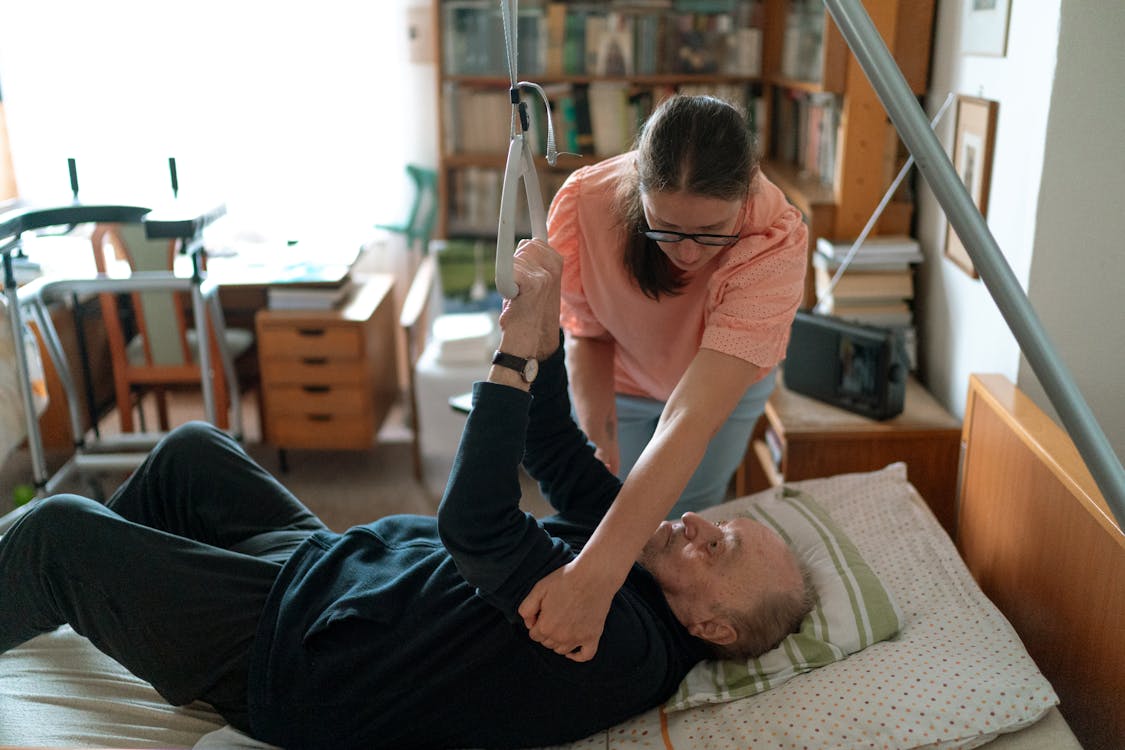 An old man exercising in bed with the help of a womanin Dallas