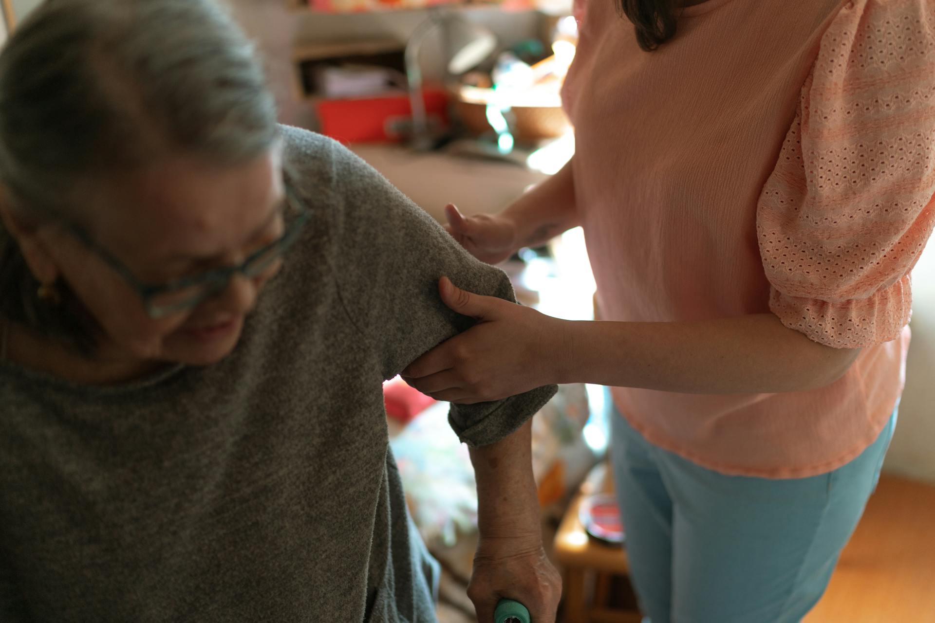 Compassionate caregiver helps elderly woman with mobility at home, offering caring support.