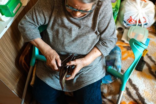 Elderly woman sitting indoors managing her wallet. Home care theme.
