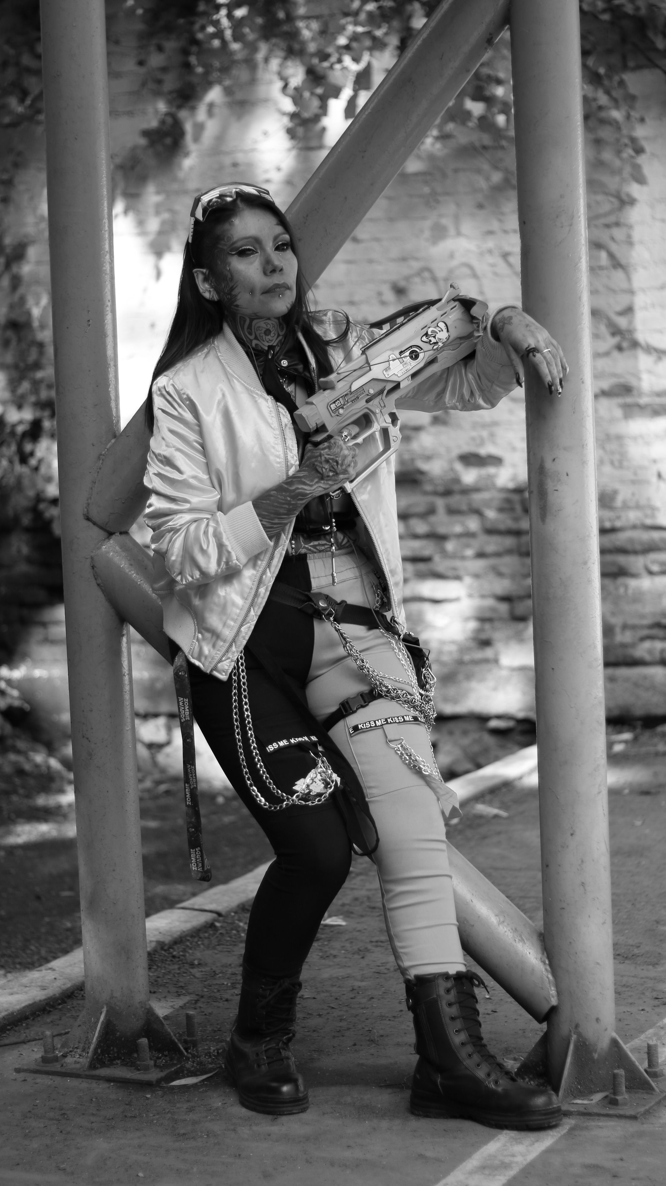 Black and white portrait of a punk woman leaning against a metal structure outdoors.