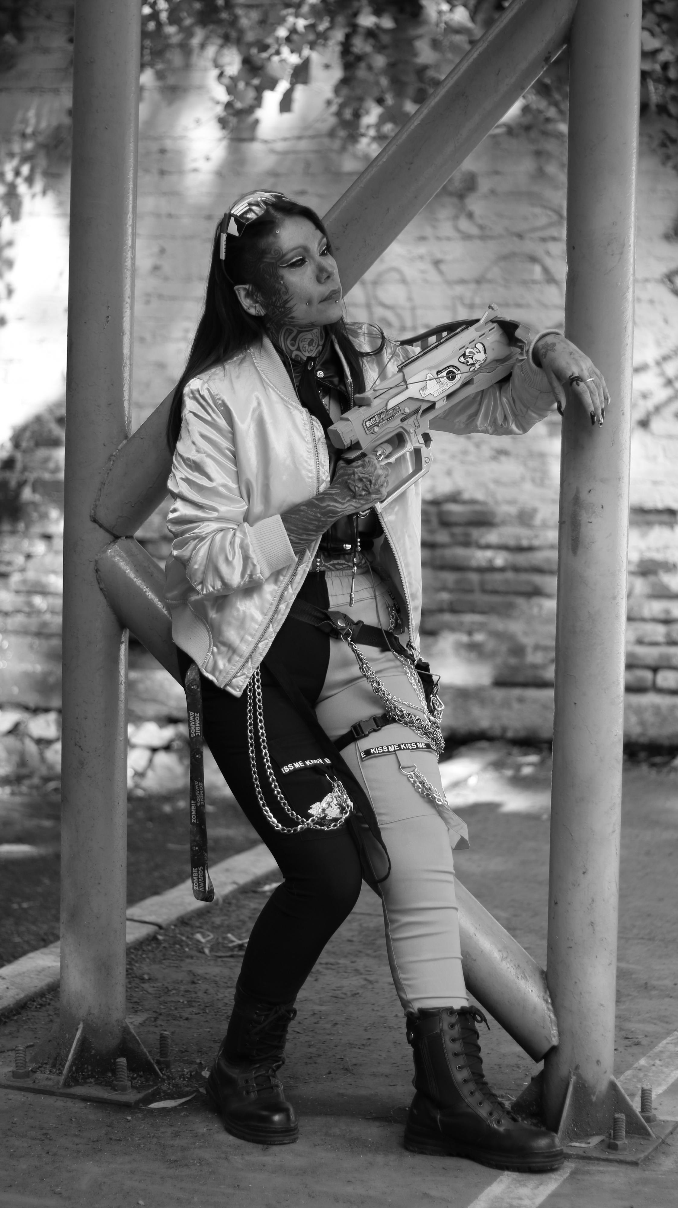 Black and white photo of a tattooed woman with a toy gun, displaying edgy style.