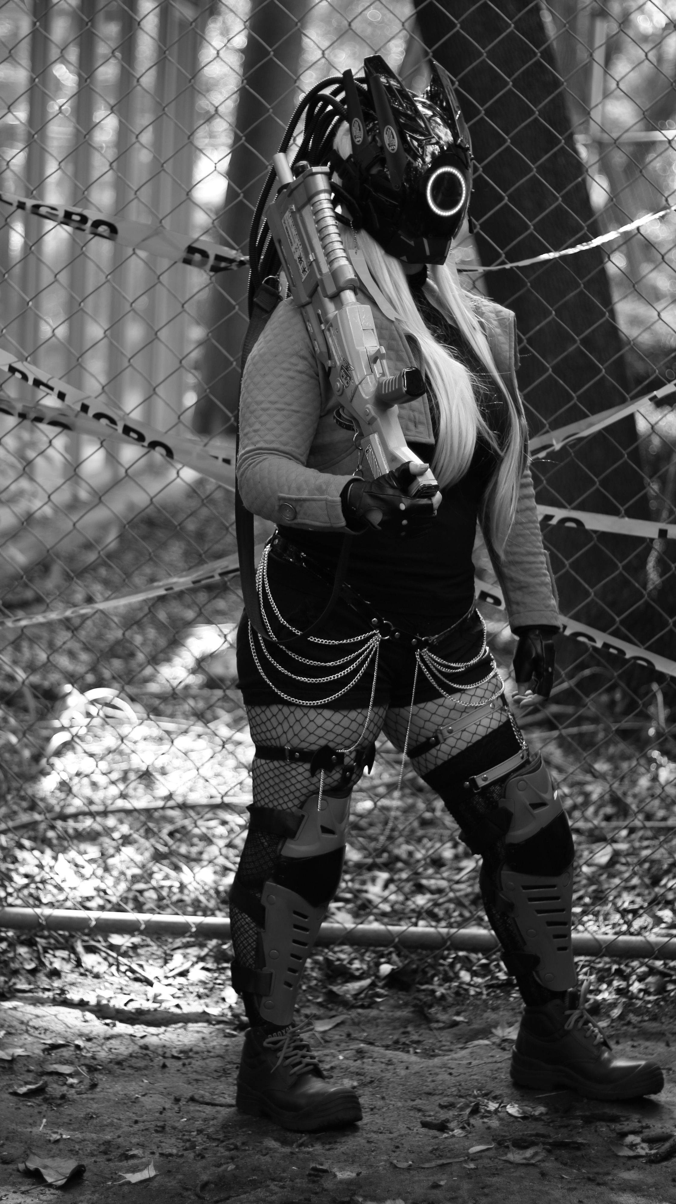 A person in cyberpunk outfit with a mask and weapon in a forest setting, black and white tone.