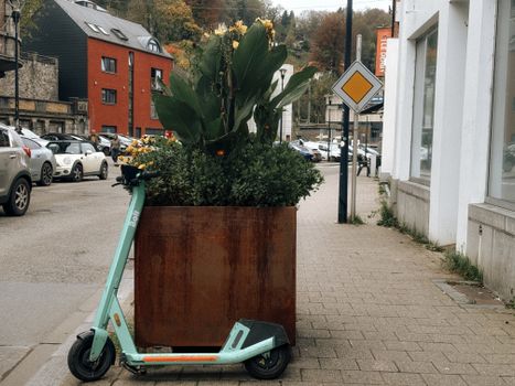 Electric scooter parked alongside large planters on a street in Dinant, Belgium.