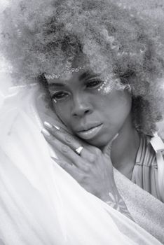 Black and white portrait of a thoughtful woman with curly hair and creative makeup, conveying introspection and grace.