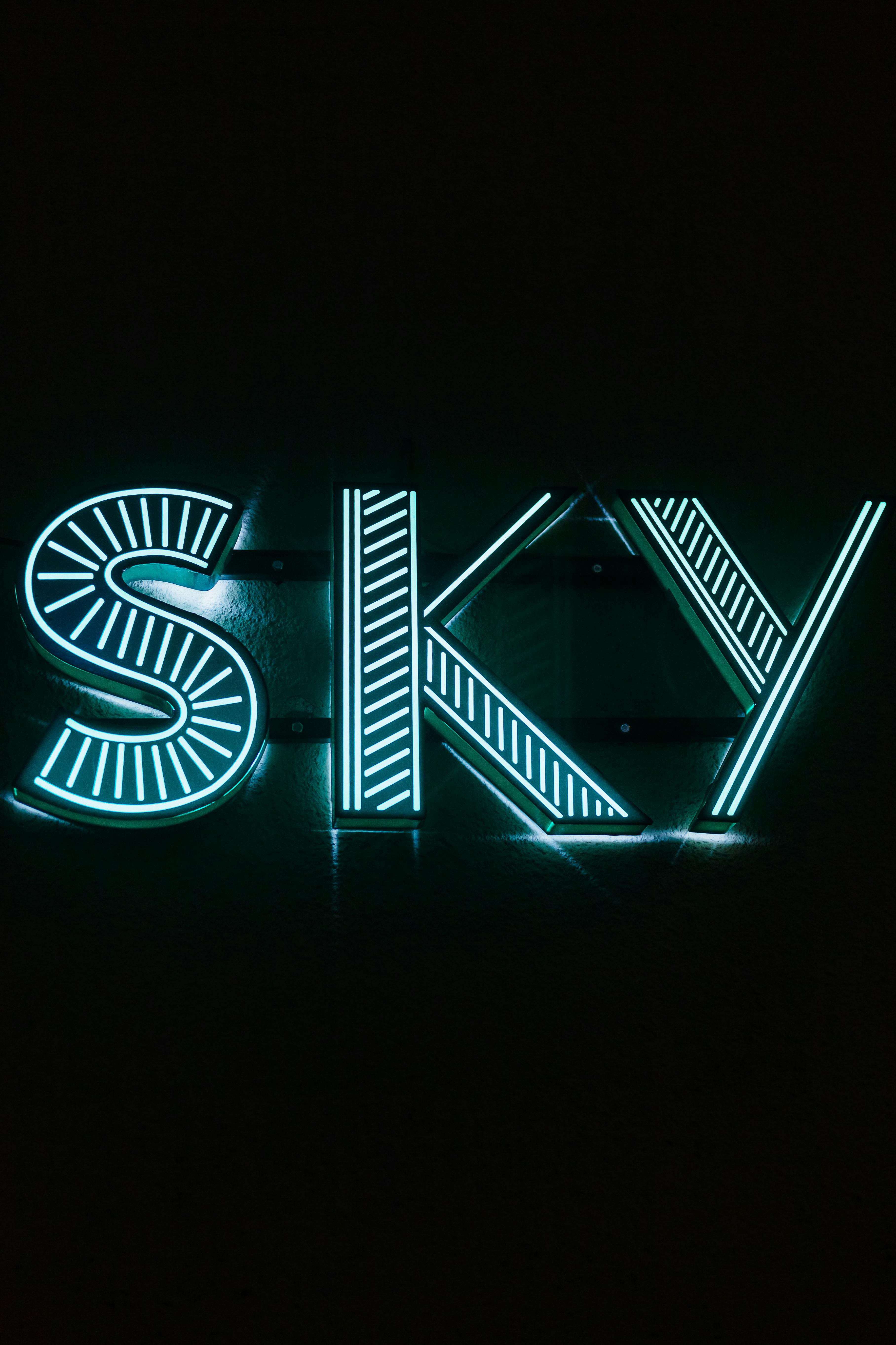 A vibrant neon sign spelling 'SKY' with glowing blue-green lights against a black background.