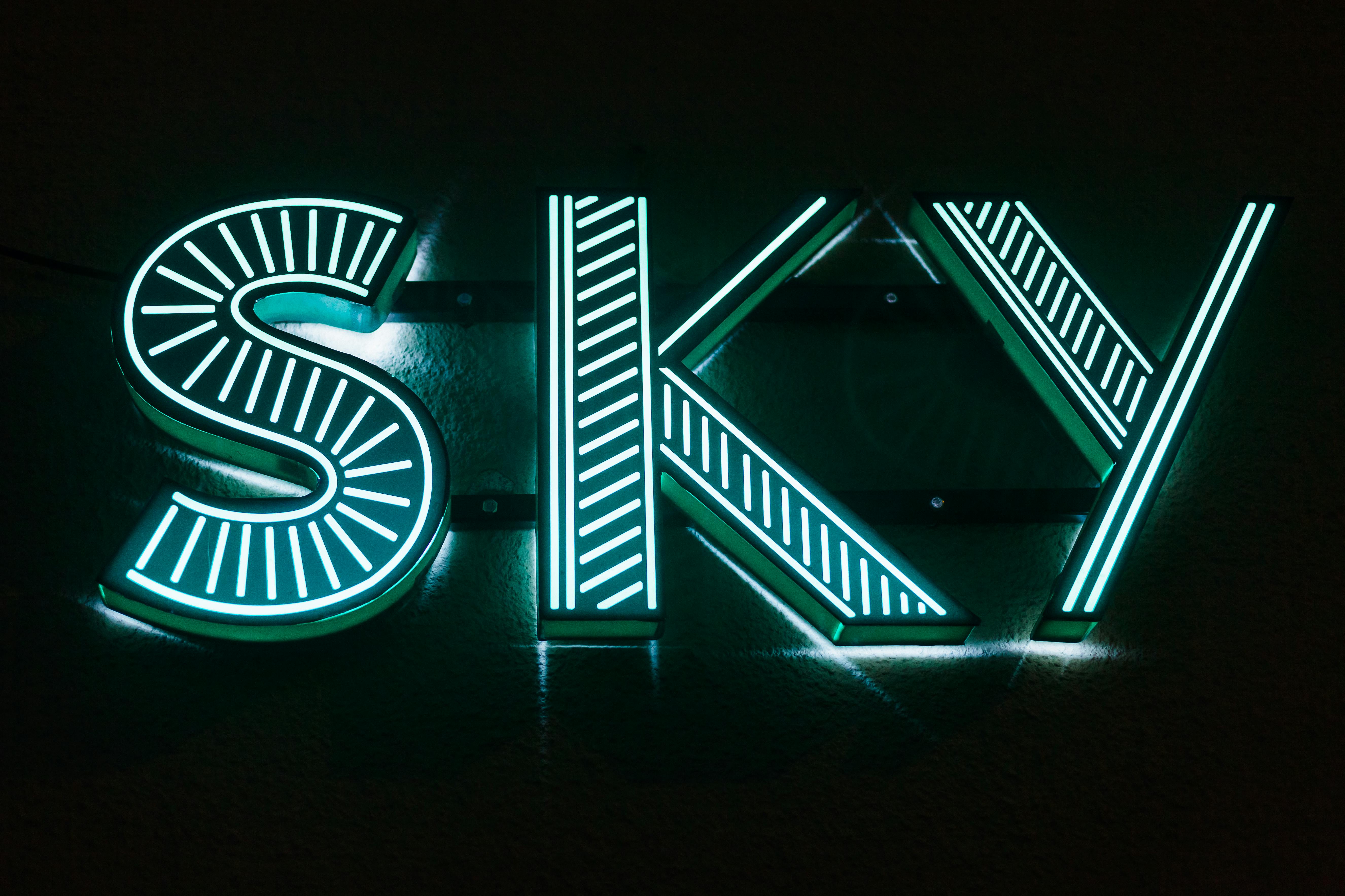 Illuminated neon sign displaying 'SKY' in a dark setting, glowing blue-green.