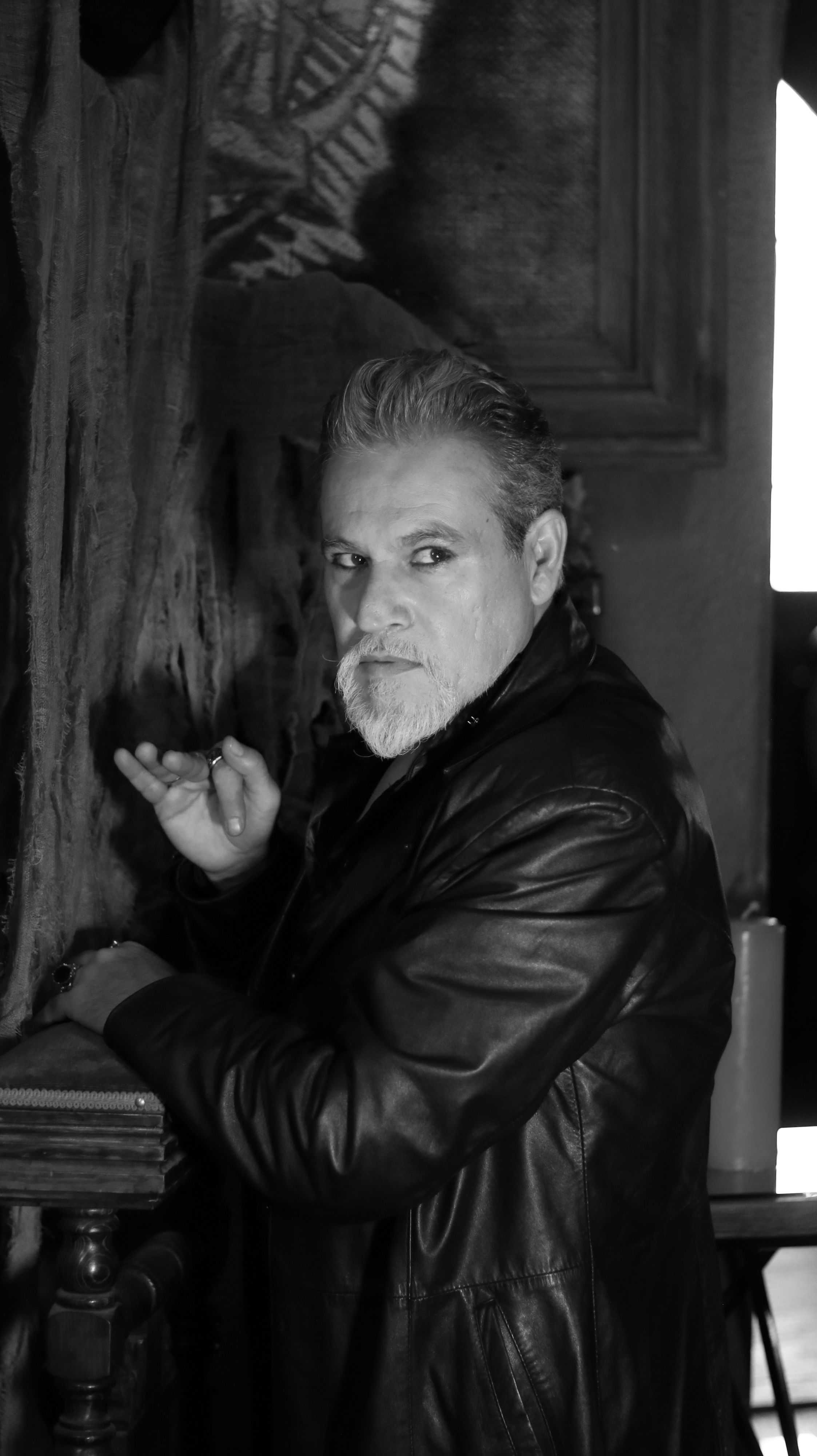 Black and white portrait of a mysterious man in a leather jacket with a deep gaze indoors.