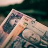 A close-up of modern British five, ten, and twenty pound banknotes fanned out against a blurred background.