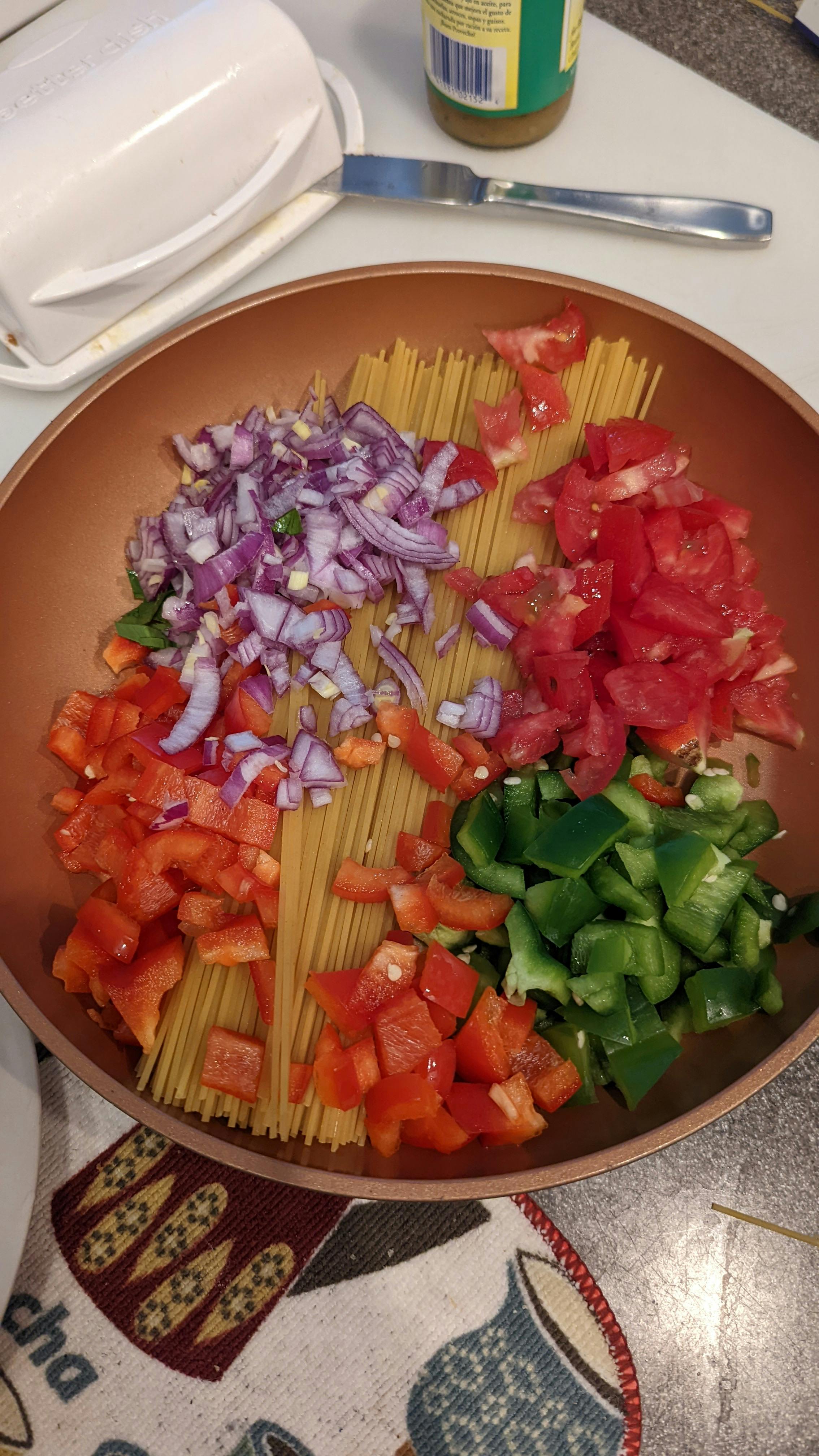 Bowl of vibrant orange-red Nigerian spaghetti jollof with colorful bell peppers and carrots, garnished with fresh parsley