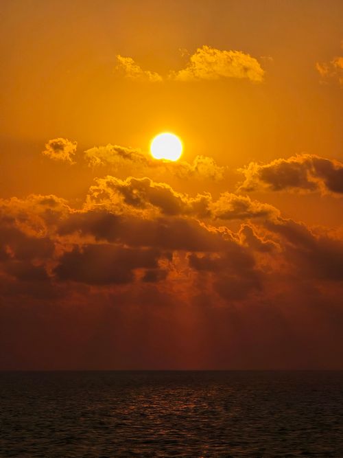 Free Golden sunset over ocean with dramatic clouds and warm tones. Stock Photo