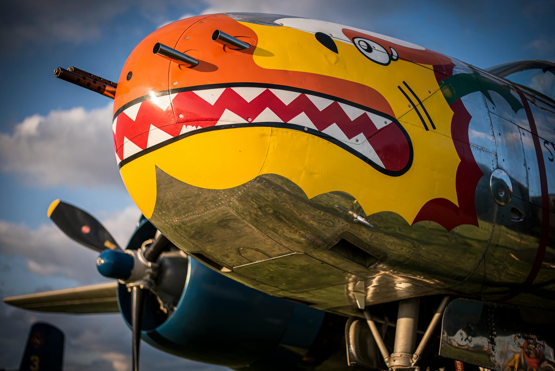 Close-up of a vibrant shark mouth painting on a historic aircraft nose cone under a sunny sky.