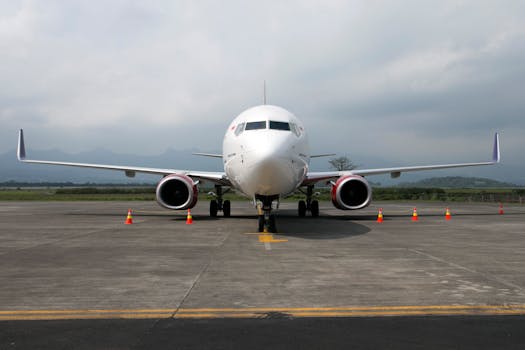 Front view of a commercial airplane parked on a runway with mountains in the background.
