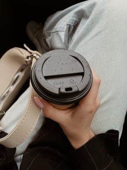 Hand holding a coffee cup with denim jeans visible, capturing a relaxed moment.