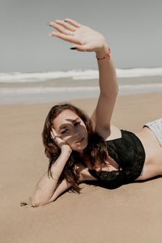 Woman in black bikini enjoying a sunny day on the beach, shielding her eyes from the sun.