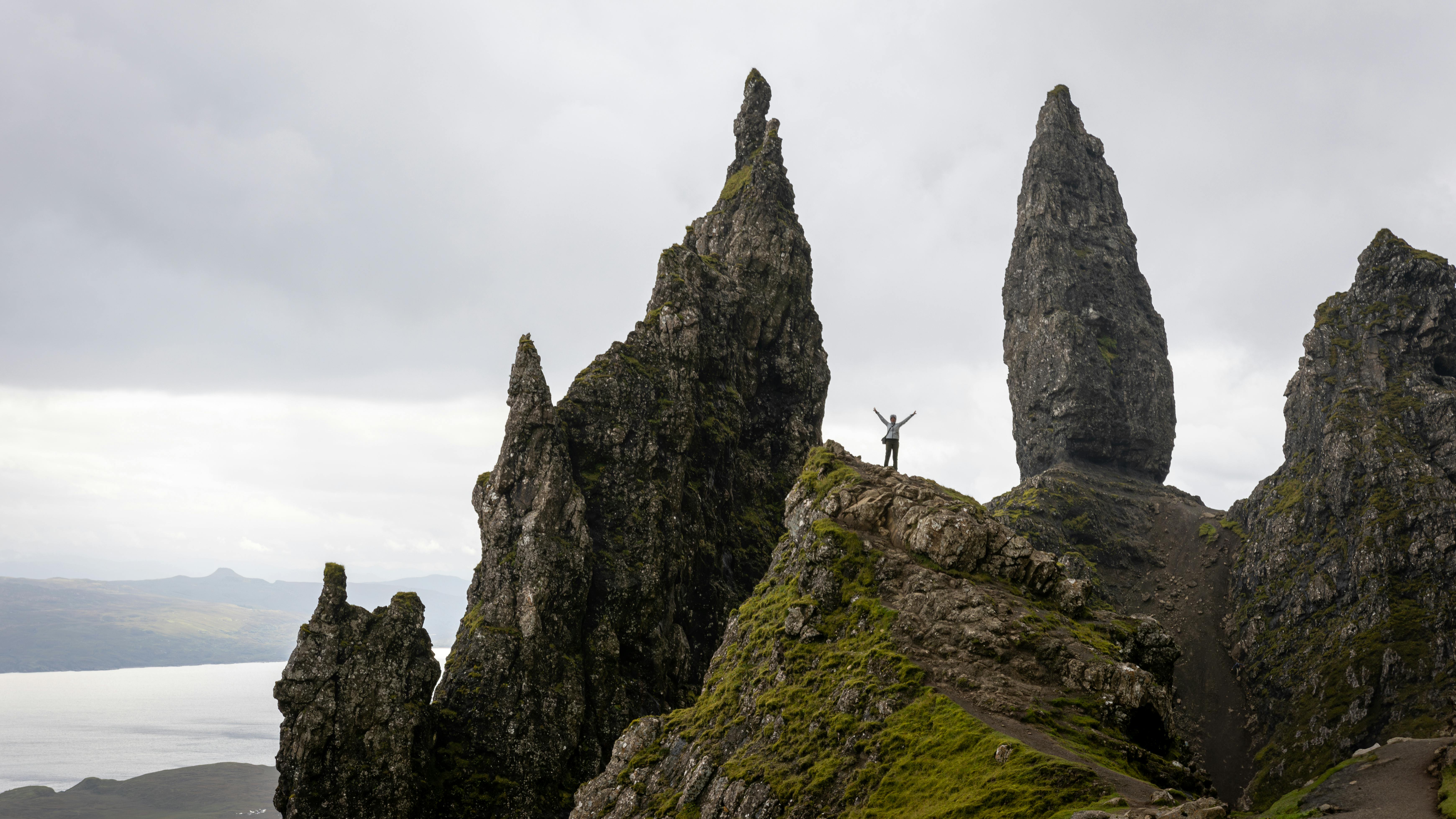 A man stands triumphantly among the towering rocks of the Old Man of Storr on the Isle of Skye.