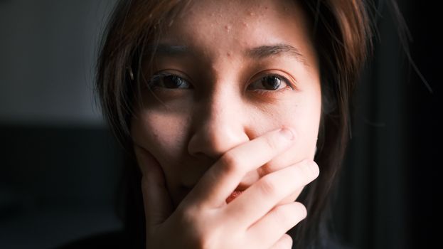 A thoughtful close-up portrait of a person covering their mouth with a hand, expressing emotion.