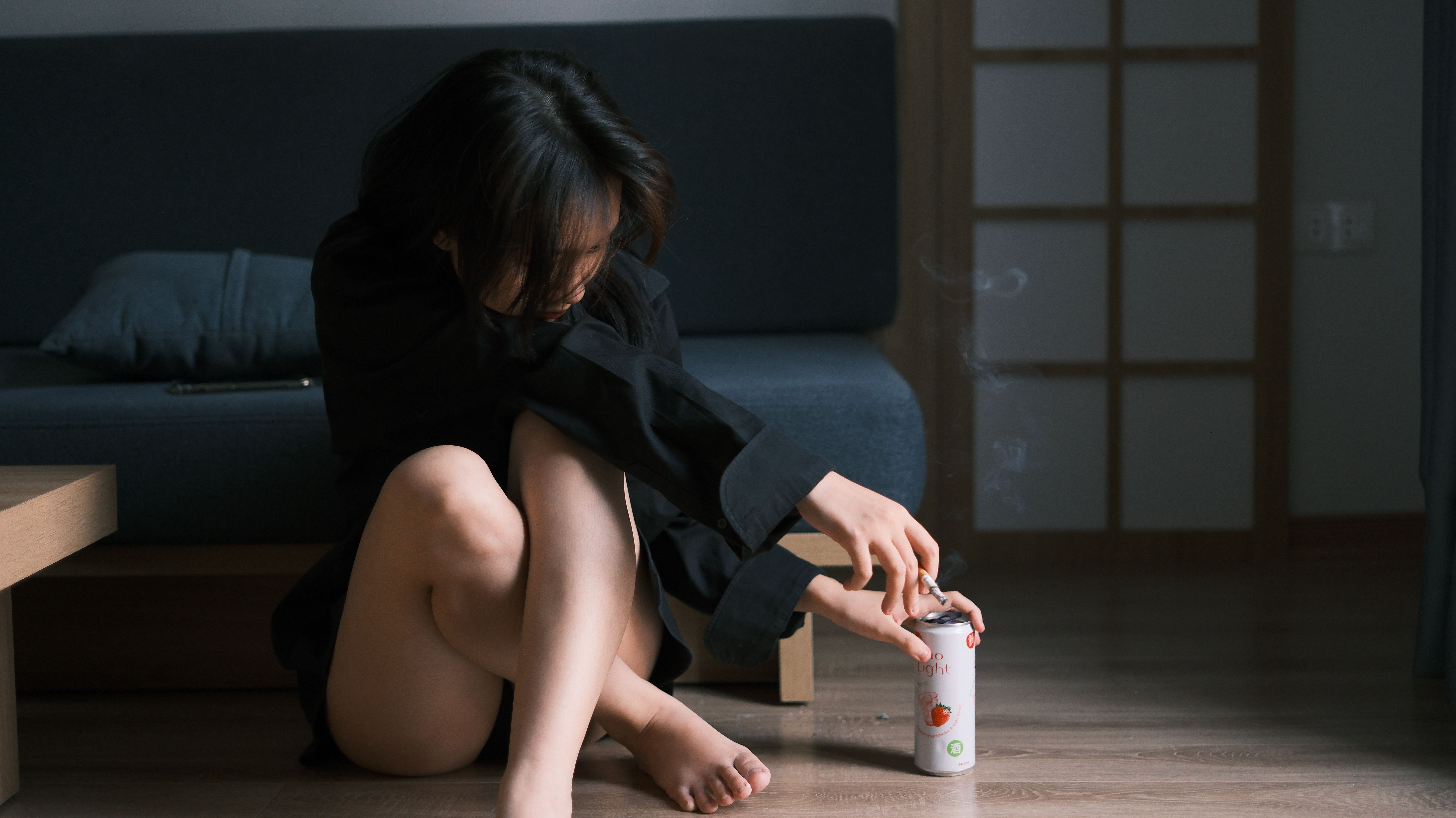A woman sitting on the floor in a contemplative pose, holding a soda can.