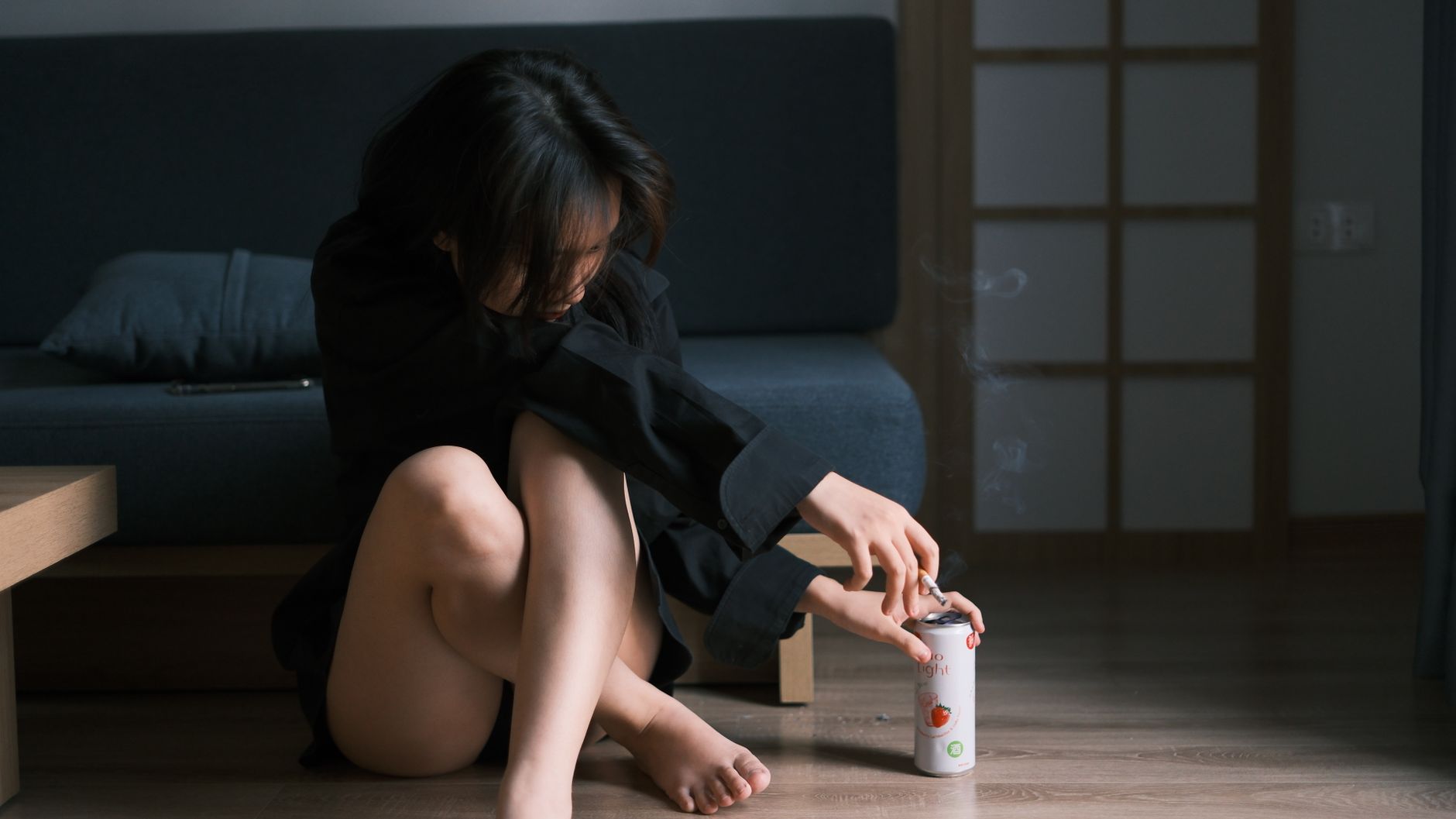 A woman sitting on the floor in a contemplative pose, holding a soda can.