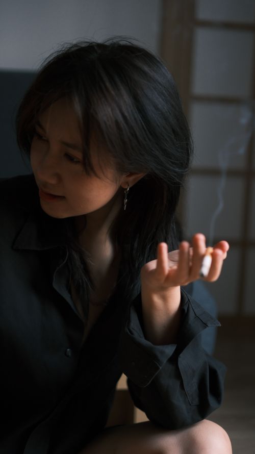 Free Woman in dark shirt enjoying a quiet moment indoors, holding a lit cigarette. Stock Photo