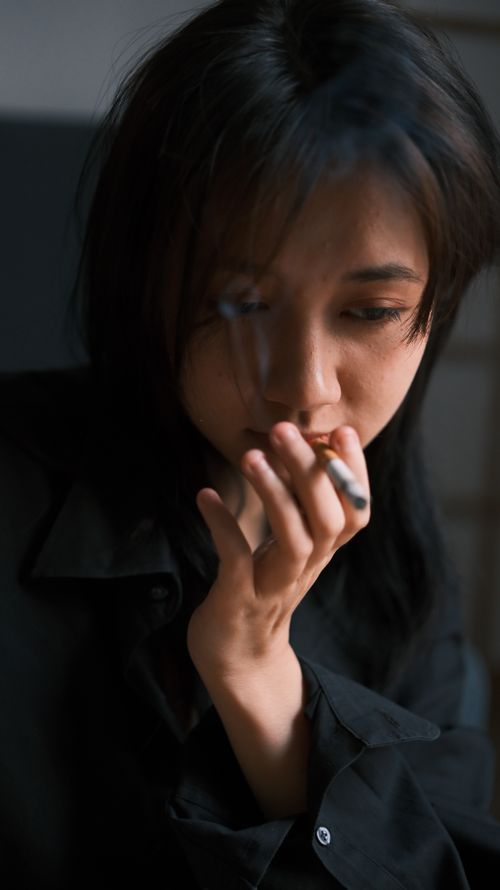 Free A young woman in deep thought holding a cigarette indoors with dim lighting. Stock Photo