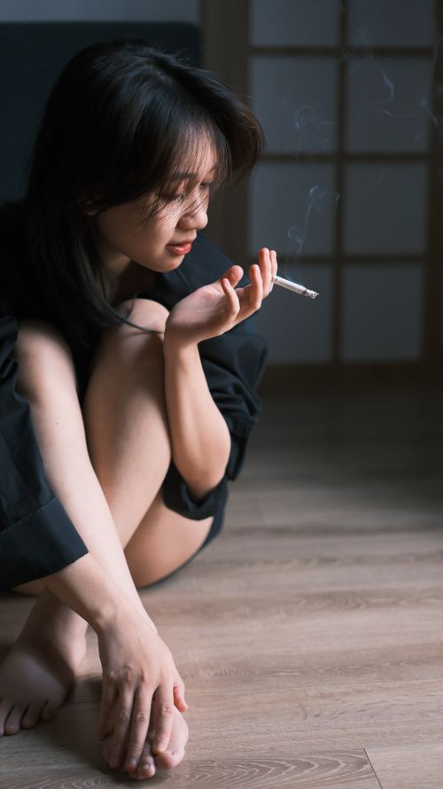 Free A woman sits thoughtfully indoors, holding a cigarette with a contemplative expression. Stock Photo