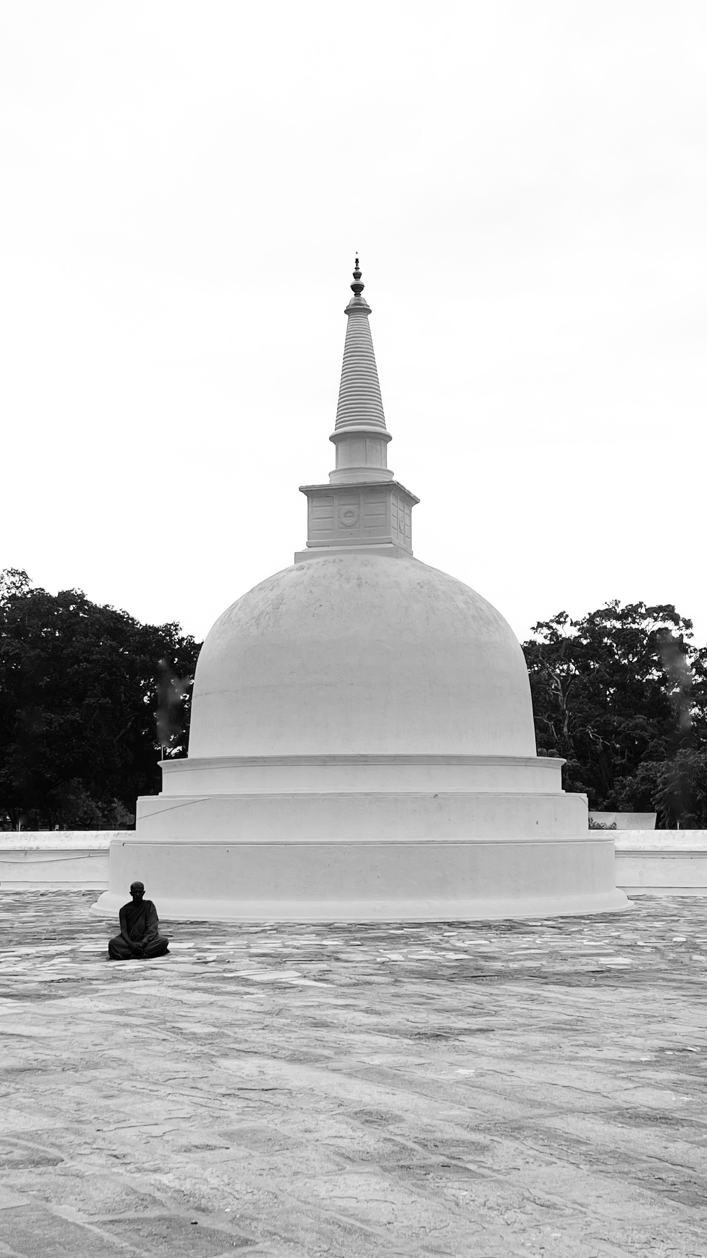 Black and white photo of a solitary person meditating by a large Buddhist stupa.