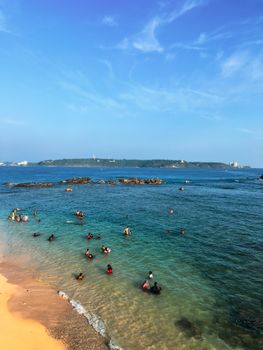 Vibrant beach scene with swimmers enjoying the ocean under a clear blue sky.