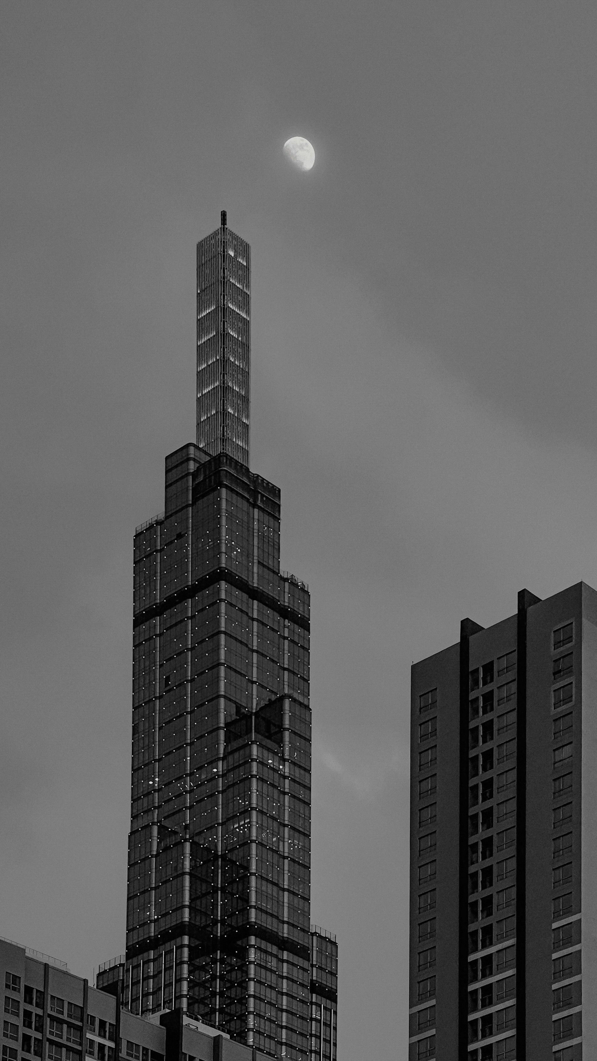 Black and white view of a prominent skyscraper in Ho Chi Minh City with the moon above.