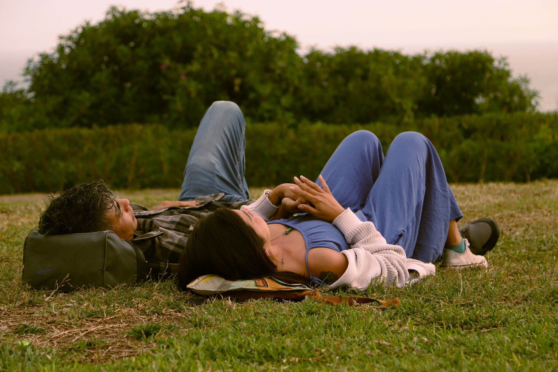 A couple enjoys a peaceful moment lying on the grass in a sunny park.