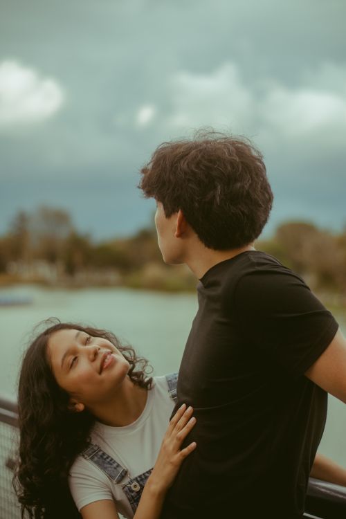 Free Young couple sharing a romantic moment by the river under cloudy skies. Stock Photo